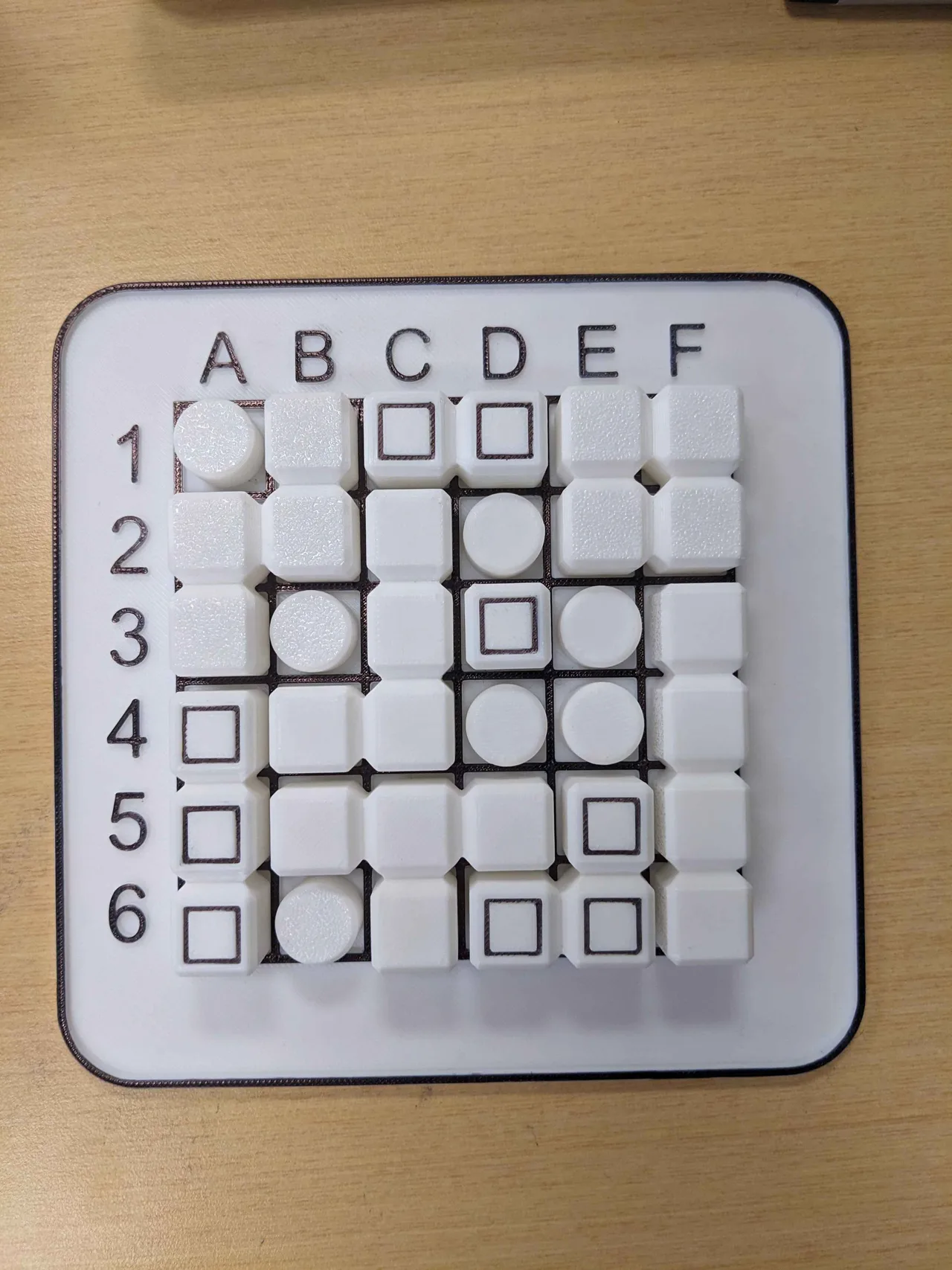 The printed six-by-six board filled with white playing pieces and square blockers
